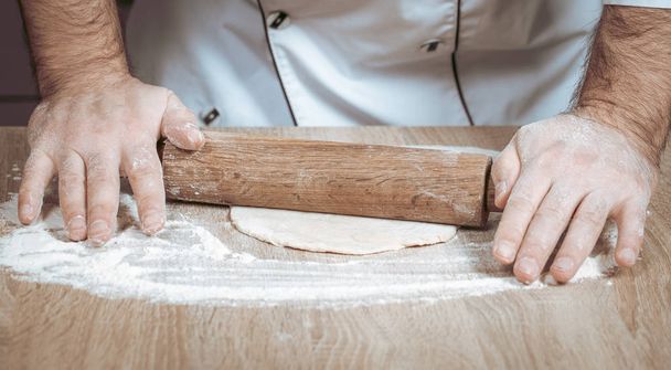 male cook kneads dough on the table - Φωτογραφία, εικόνα