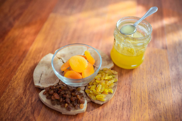 Изюм, сушеные абрикосы и мед на столе
 - Фото, изображение
