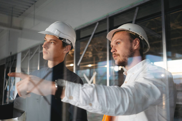 Yapı denetçisi elinde planı tutun ve endüstriyel şantiyede güvenlik sert şapka giyen işçi ile toplantı var. Mimar ve yapı mühendisi proje çizimi tartışmak - Fotoğraf, Görsel