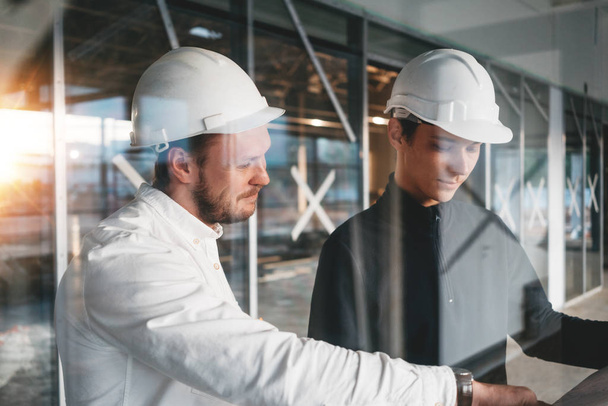 Building engineer and worker hold blueprint in hand while discussong construction site. Industrial engineers have meeting on build - Valokuva, kuva