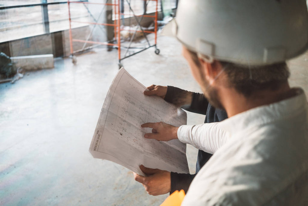 Building inspector hold blueprint in hand and have meeting with worker wearing safety hard hat on industrial construction site. Architect and build engineer discuss project drawing - Foto, Imagem