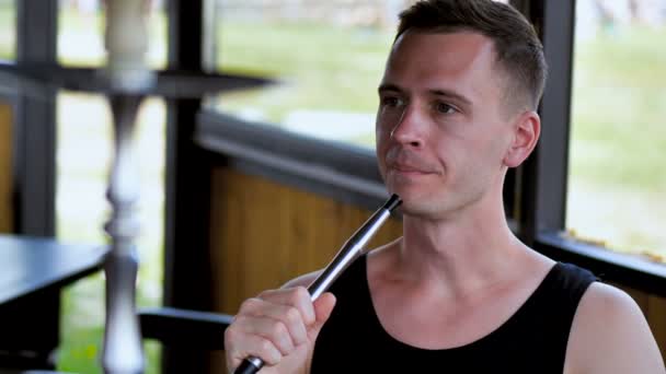 Genç adam plaja yakın yaz günü bir oryantal restoranda bir nargile sigara eğleniyor - Video, Çekim