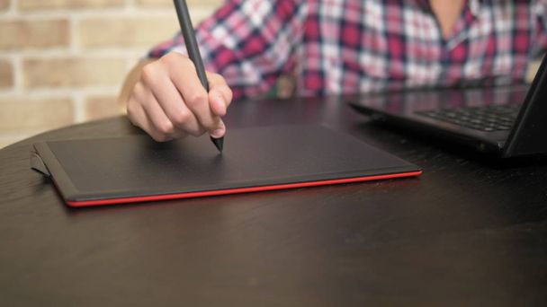 schließen. Hand eines halbwüchsigen Jungen im karierten Hemd mit einem Stift. funktioniert auf einem Grafik-Tablet - Foto, Bild