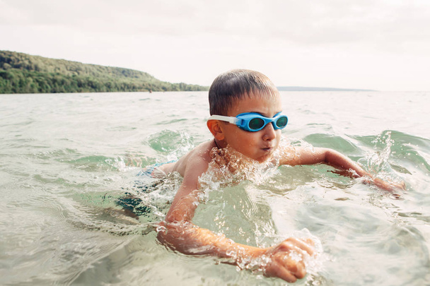 Симпатичні смішні кавказькі хлопчик купання в озері Рівер з підводними окуляри. Дитячий дайвінг у воді на пляжі. Автентичний справжній спосіб життя щасливого дитинства. Літня забава відкритий водної активності. - Фото, зображення