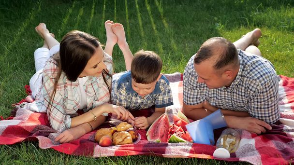happy family members lie on stomach on red blanket at picnic - Photo, Image