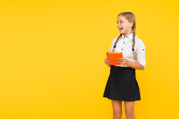 The joy of good knowledge. Cute small girl holding book on yellow background. Adorable little schoolchild getting knowledge from book. Knowledge and skills. Knowledge day or September 1, copy space - Foto, imagen