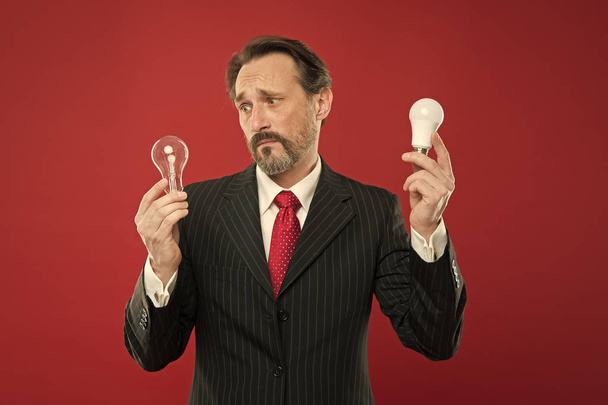 Symbol of idea progress and innovation. Idea for business. Environment friendly idea. Genius idea. Light up your business. Man bearded businessman formal suit hold light bulb on red background - Photo, Image