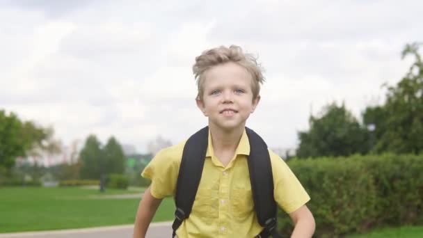 Happy little boy with backpack running in park, slow motion. Back to school concept - Video