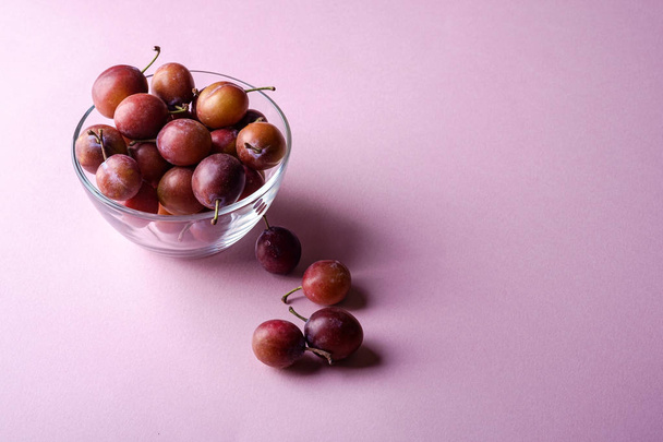 Fruits de prunes sucrés mûrs dans un bol en verre proche avec des prunes éparses sur fond rose, lumière douce, espace de copie
 - Photo, image