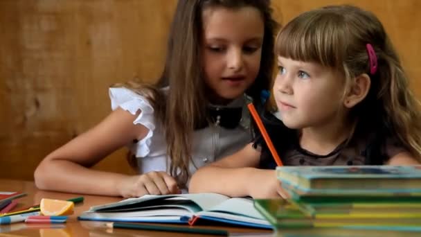 twee kleine schoolmeisjes fluisteren zittend aan de balie - Video