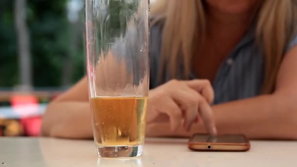 op de achtergrond van een glas met een koolzuurhoudende sinaasappel drank beweegt de hand van de vrouw op een smartphone - Video
