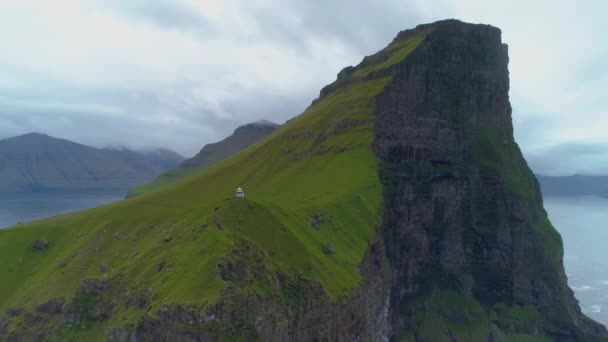Aerial, Time Warp: Vliegen weg van een steile grasheuvel en zwarte klif op een bewolkte ochtend op de Faeröer Eilanden. Wandelaars staan aan de rand van majestueuze kliffen kijken naar spectaculaire oceaan onder hen. - Video