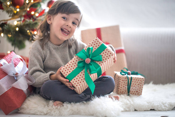 Menina bonita está segurando uma caixa de presente e sorrindo enquanto sitti
 - Foto, Imagem