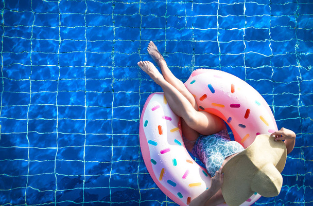 Una mujer en un sombrero se relaja en un círculo inflable en la piscina
. - Foto, imagen