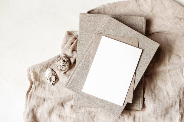 Feminine stationery, desktop mock-up scene. Blank greeting card, craft envelope, sea shells and old books on beige linen tablecloth background. Flat lay, top view. Summer rustic composition. - Foto, Imagen