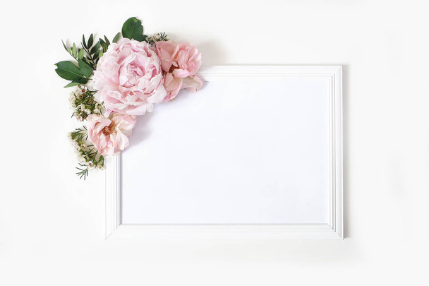 Wedding, birthday sign board mock-up scene. Blank white wooden frame. Decorative floral corner. Green leaves, pink peony, roses and wax flowers. White table background. Flat lay, top view. - Foto, immagini