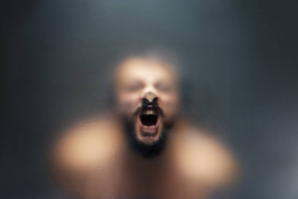 Creepy looking man is screaming behind a frosted glass. - Foto, Bild