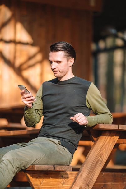 Šťastný muž si na svém telefonu zadáváním vzkaz a zároveň relaxuje venku ve městě. - Fotografie, Obrázek