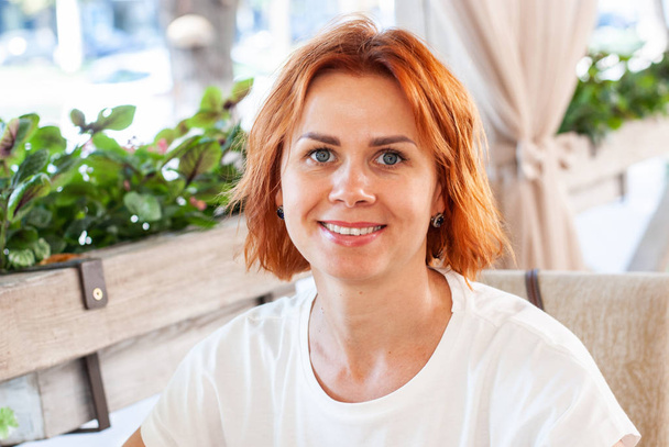 Una giovane ragazza con i capelli rossi sorride mentre si siede a un tavolo a un
  - Foto, immagini