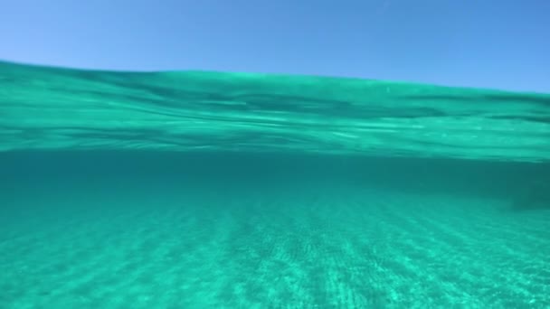 Slow Motion, Half Underwater: Εντυπωσιακή λήψη του μακρινού νησιού στη μέση του κρυστάλλινου ωκεανού σε μια ηλιόλουστη μέρα το καλοκαίρι. Awesome μισό υποβρύχια θέα της αμμώδους πυθμένα του ωκεανού και τη Σαρδηνία. - Πλάνα, βίντεο