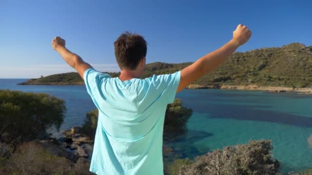 Slow Motion Close Up: Ecstatic mannelijke toerist viert het bereiken van een schilderachtig uitzichtpunt in spectaculair Sardinië. Onherkenbare jongeman strekt zijn armen uit terwijl hij het pittoreske Italiaanse strand observeert - Video