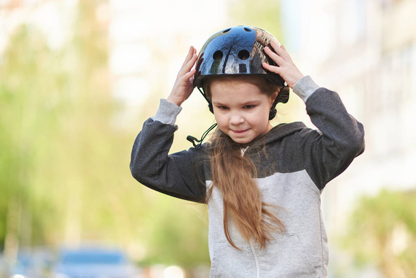 小さな女の子はスケートボードに乗っている間、彼女のヘルメットをまっすぐにします. - 写真・画像