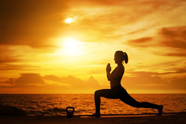 nő gyakorló jóga közben szürreális naplemente a tengerparton. - Fotó, kép