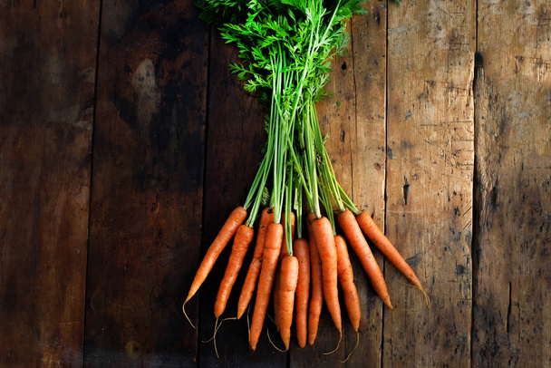 органическая морковь с зеленой морковкой вершины на деревенском деревянном столешнице, домашний выращенный, растительный на основе, сверху вид, горизонтальный формат с копировальным пространством
 - Фото, изображение