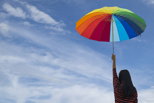 Νέα γυναίκα κρατώντας πολύχρωμο ομπρέλα στο γαλάζιο του ουρανού - Φωτογραφία, εικόνα