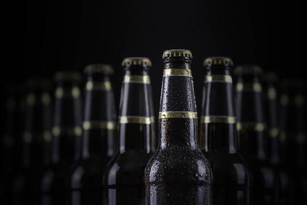 Bouteilles de bière avec des étiquettes vierges alignées en mise au point sélective sur fond noir, une avec des gouttelettes de gel
 - Photo, image