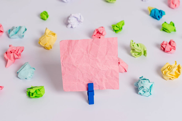 Colored crumpled sheets placed around the empty rectangle square shaped reminder note in the centre of a white floor. Office supplies, blank paper pinned by a fastener. - Photo, Image