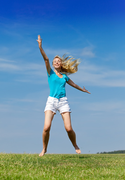 La femme heureuse saute dans un champ vert d'été contre le ciel bleu
 - Photo, image