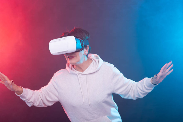 Χαμογελάστε χαρούμενη γυναίκα να πάρει εμπειρία χρησιμοποιώντας VR γυαλιά κεφαλής εικονικής πραγματικότητας σε κόκκινο-μπλε φόντο - Φωτογραφία, εικόνα