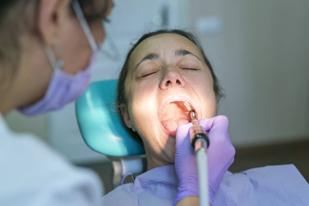 Οδοντίατρος και ασθενής στο οδοντιατρείο. Κοντινό στο Οδοντιατρικό τρυπάνι χρήση για τα δόντια του ασθενούς στο γραφείο οδοντιατρικής σε μια διαδικασία οδοντιατρικής θεραπείας. Γυναίκα που έχει δόντια που εξετάζονται στους Οδοντίατροι - Φωτογραφία, εικόνα