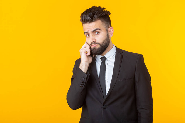 Resmi kıyafetler içinde sakallı sevimli genç adam sarı bir arka plan üzerinde poz telefonda konuşurken. Gayri resmi toplantı ve iş anlaşması kavramı. - Fotoğraf, Görsel