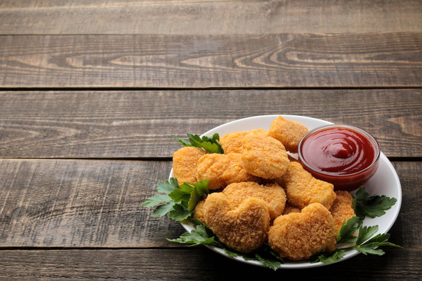 Nuggets z kurczaka z czerwonym sosem na talerzu na brązowym drewnianym stole. Fast food. miejsce na tekst - Zdjęcie, obraz