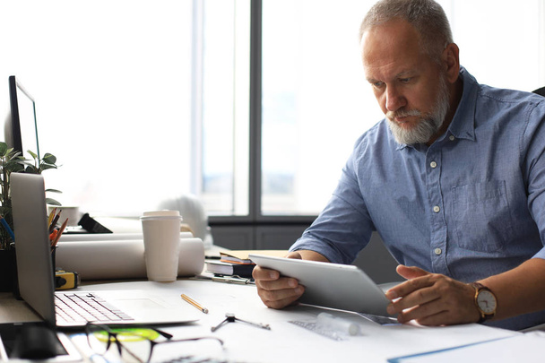 Reifer Geschäftsmann arbeitet mit digitalem Tablet im modernen Büro. - Foto, Bild