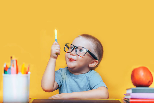 Niño pequeño pintando y haciendo deberes en su escritorio teniendo una idea, concepto de inspiración. volver a la escuela sobre fondo amarillo
 - Foto, Imagen