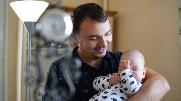 ランプで家で赤ちゃんを抱いている愛情のある若者の肖像画. - 写真・画像