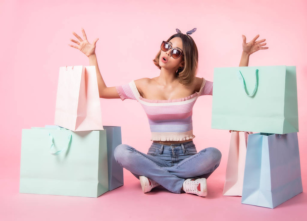Asian pretty young woman walking over pink  pastel background. She smiling and  holding shopping bags. she nice-looking lovely attractive shine . - Foto, Imagen