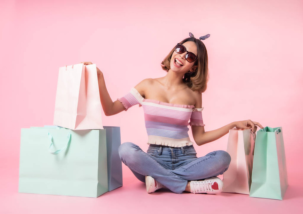 Asian pretty young woman walking over pink  pastel background. She smiling and  holding shopping bags. she nice-looking lovely attractive shine . - Foto, Bild