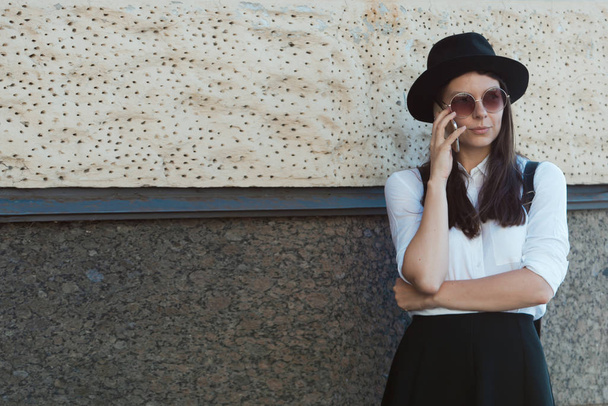 young woman in a hat and a white shirt walks in the city and uses a smartphone. - 写真・画像