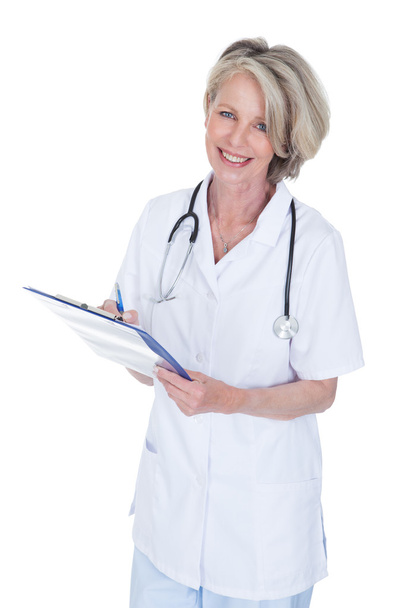 Mature Female Doctor Writing On Clipboard - Photo, Image