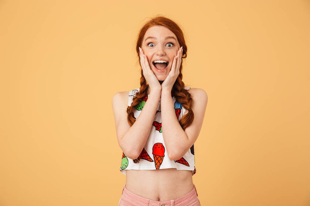 Excited beautiful redhead woman dressed in ice cream printed t-shirt posing isolated over yellow background. - Photo, Image
