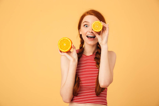 Mutlu genç güzel kızıl saçlı kadın turuncu tutan sarı arka plan üzerinde izole poz. - Fotoğraf, Görsel