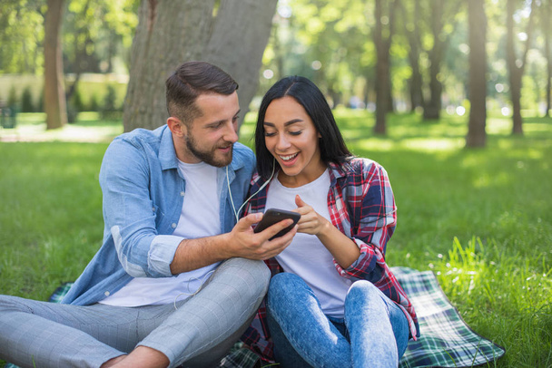 kochająca para siedzi na kocu Plaid w parku i korzystać z telefonu, przystojny facet i dziewczyna - Zdjęcie, obraz
