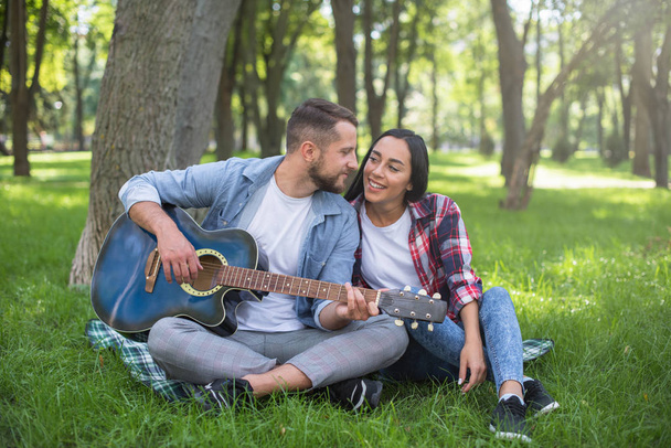 guy and girl play the guitar in the park, sit on the grass near the tree - Fotografie, Obrázek