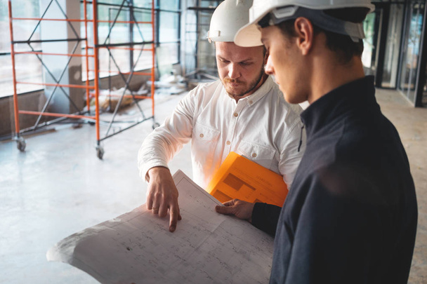 Close up view on construction drawing in engineer hands. Builder discussing blueprint with architect building under construction - Fotografie, Obrázek