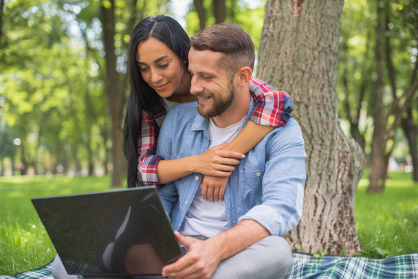 parkta sevgi dolu çift bir dizüstü bilgisayar kullanıyor, sarılma - Fotoğraf, Görsel