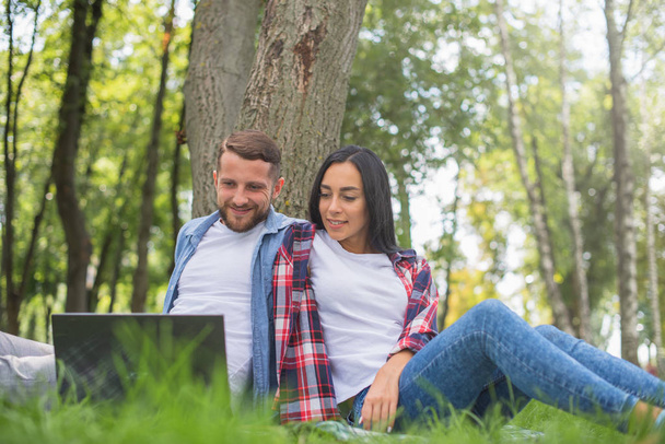 αγαπημένο ζευγάρι στο πάρκο χρησιμοποιούν ένα φορητό υπολογιστή, αγκαλιές - Φωτογραφία, εικόνα